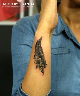 Tatouage plume avec deux fleurs sur l'avant bras